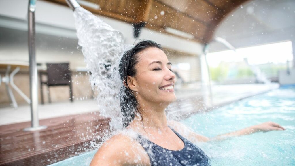 femme à la piscine dans l'eau qui profite de l’hydrothérapie avec un jet d'eau